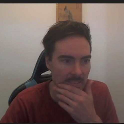 a man with a mustache is sitting in a chair with his hand on his chin .
