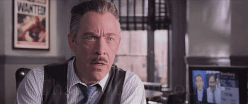A Man With A Mustache Is Sitting In Front Of A Poster That Says Wanted GIF