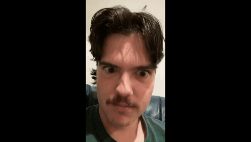 A Man With A Mustache Is Sitting On A Couch . GIF