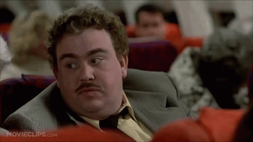 A Man With A Mustache Is Sitting On An Airplane Looking At Something . GIF