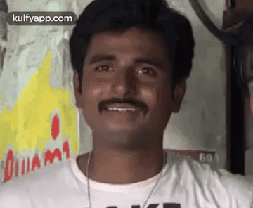 A Man With A Mustache Is Smiling For The Camera While Wearing A White Shirt . GIF