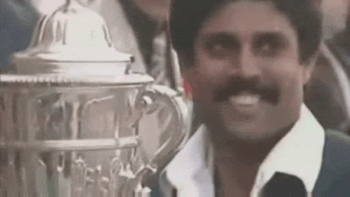 A Man With A Mustache Is Smiling While Holding A Trophy In Front Of Him . GIF