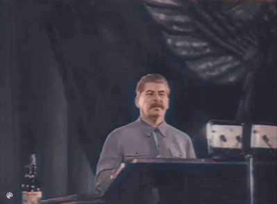 A Man With A Mustache Is Standing At A Podium Giving A Speech In A Dark Room . GIF