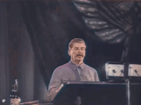 A Man With A Mustache Is Standing At A Podium Giving A Speech In A Dark Room . GIF
