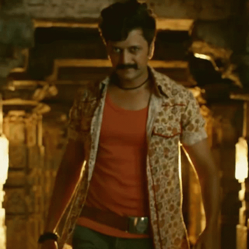 A Man With A Mustache Is Standing In A Dark Room With A Light Shining On Him GIF