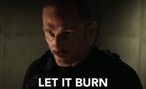 A Man With A Mustache Is Standing In A Dark Room With The Words `` Let It Burn '' Written On The Screen . GIF