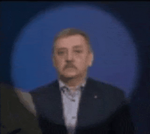 A Man With A Mustache Is Standing In Front Of A Blue Light . GIF