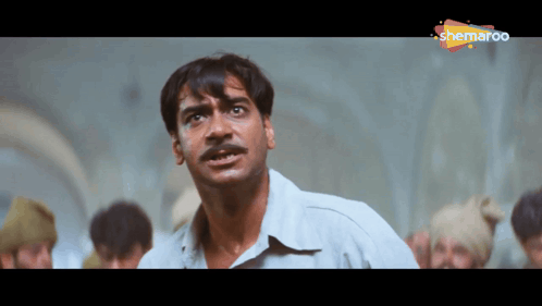 A Man With A Mustache Is Standing In Front Of A Group Of People And A Sign That Says Shemaroo On It GIF