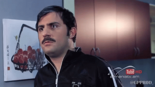 A Man With A Mustache Is Standing In Front Of A Painting That Says Tube Hd GIF