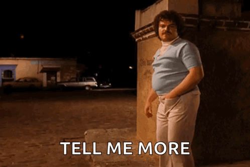 A Man With A Mustache Is Standing Next To A Wall With The Words Tell Me More Below Him GIF