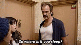 A Man With A Mustache Is Standing Next To A Woman In A Room And Talking To Her . GIF