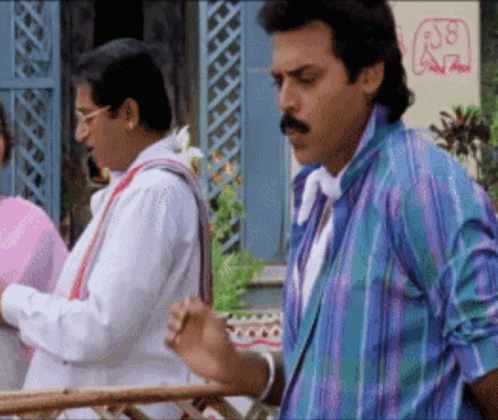 A Man With A Mustache Is Standing Next To Another Man In A Colorful Shirt . GIF