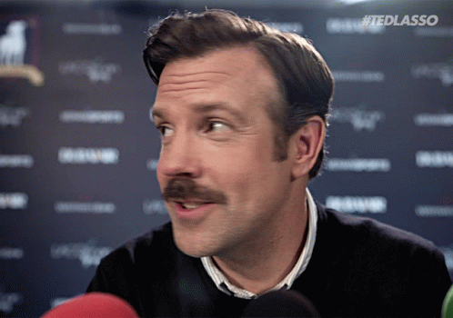 A Man With A Mustache Is Talking Into A Microphone With #Tedlasso Written On The Bottom Right GIF