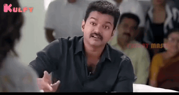 A Man With A Mustache Is Talking To A Woman While Sitting In Front Of A Crowd Of People . GIF