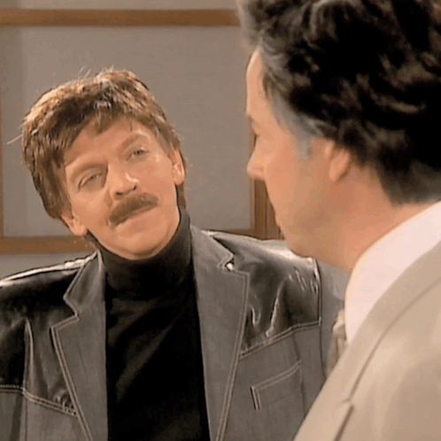 A Man With A Mustache Is Talking To Another Man GIF