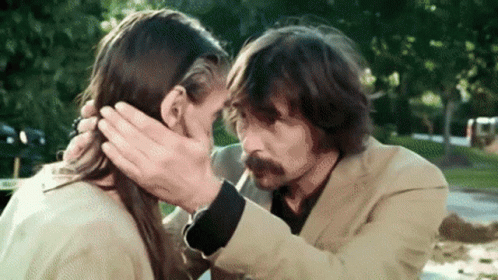 A Man With A Mustache Is Touching A Woman 'S Face . GIF