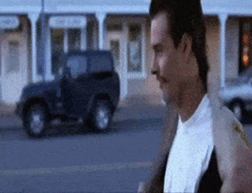 A Man With A Mustache Is Walking Down A Street In Front Of A Jeep . GIF