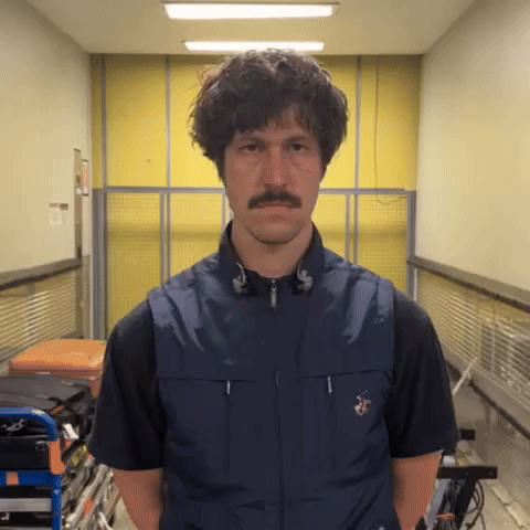 a man with a mustache is wearing a blue vest and black shirt