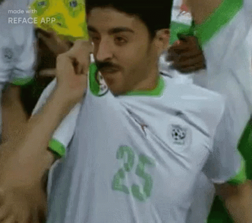 A Man With A Mustache Is Wearing A White And Green Soccer Jersey With The Number 25 On The Front . GIF