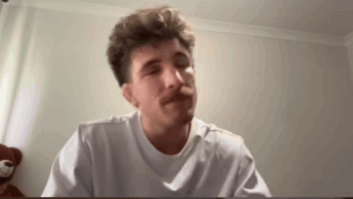 A Man With A Mustache Is Wearing A White T-Shirt And Making A Funny Face . GIF