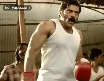 A Man With A Mustache Is Wearing Boxing Gloves And A Tank Top . GIF