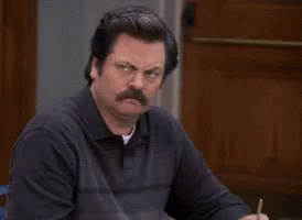 A Man With A Mustache Sits At A Table With A Pen In His Hand GIF