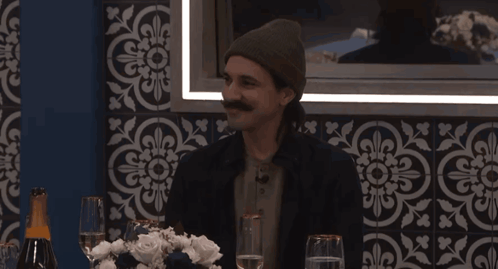 a man with a mustache sits at a table with wine glasses