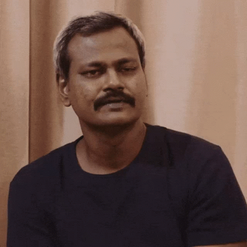 A Man With A Mustache Wearing A Black Shirt Looks At The Camera GIF