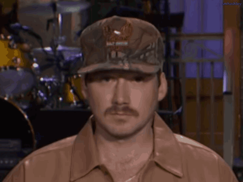 A Man With A Mustache Wearing A Hat And A Leather Jacket . GIF
