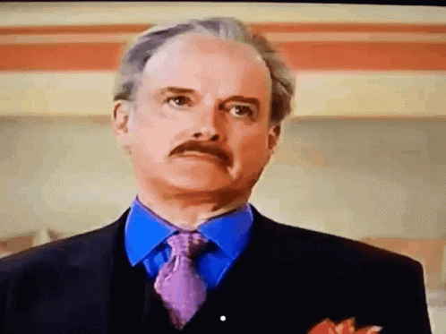 A Man With A Mustache Wearing A Suit And Tie Looks At The Camera GIF