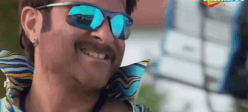 A Man With A Mustache Wearing Sunglasses And A Colorful Shirt Is Smiling . GIF