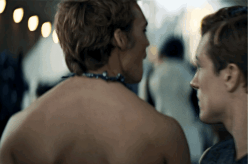 A Man With A Necklace Around His Neck Is Looking At Another Man GIF