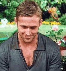 A Man With A Necklace Around His Neck Is Smiling While Sitting In Front Of A Flower Pot . GIF
