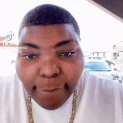 A Man With A Nose Ring Is Making A Funny Face While Wearing A White Shirt And A Gold Chain . GIF