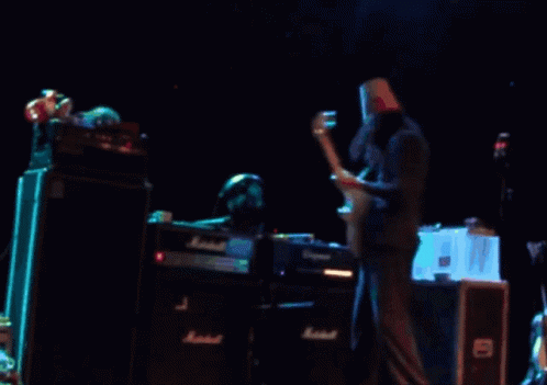 A Man With A Paper Bag On His Head Is Playing A Guitar In Front Of A Marshall Amplifier GIF
