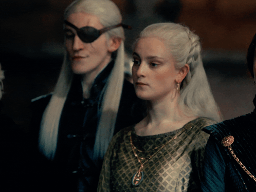A Man With A Pirate Eye Patch And A Woman In A Green Dress Are Standing Next To Each Other GIF