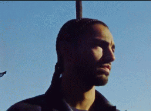 A Man With A Ponytail Is Standing In Front Of A Pole GIF