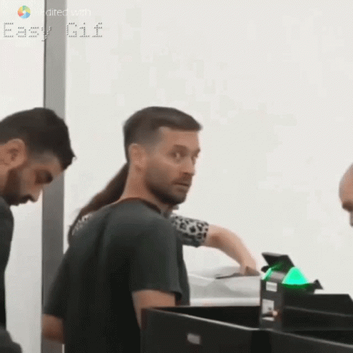 A Man With A Ponytail Is Standing Next To A Woman At A Counter . GIF