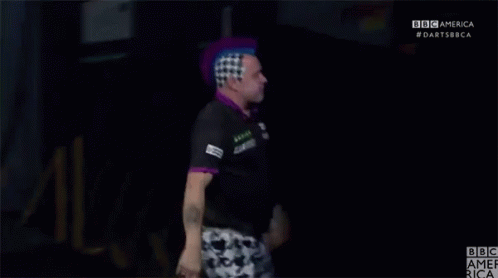 A Man With A Purple Mohawk Stands In Front Of A Bbc America Logo GIF