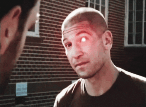A Man With A Red Eye Is Talking To Another Man In Front Of A Brick Building GIF