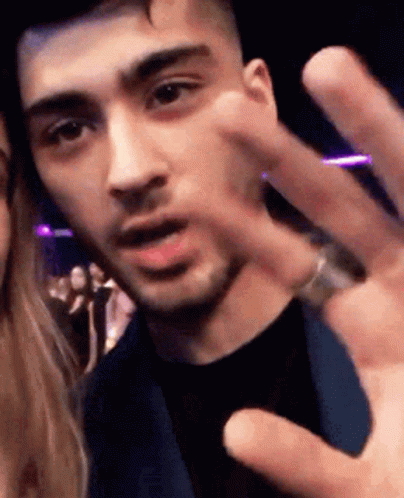 A Man With A Ring On His Finger Is Giving A Peace Sign To A Woman . GIF