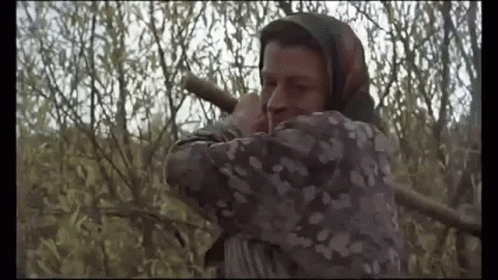 A Man With A Scarf Around His Head Is Holding A Rifle In A Field . GIF