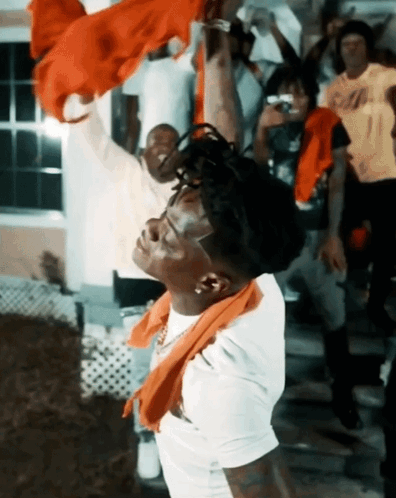 A Man With A Scarf Around His Neck Is Standing In Front Of A Crowd GIF