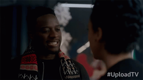 A Man With A Scarf Around His Neck Smiles While Talking To A Woman With #Uploadtv Written Below Him GIF