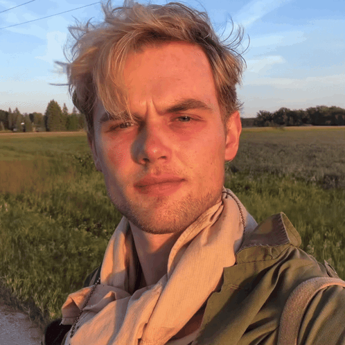 A Man With A Scarf Around His Neck Stands In A Field GIF