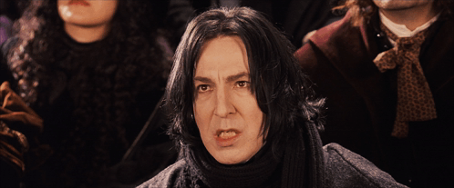 A Man With A Scarf Around His Neck Stands In Front Of A Group Of People GIF