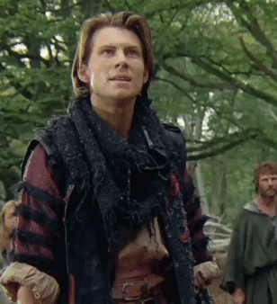 A Man With A Scarf Around His Neck Stands In The Woods GIF
