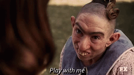A Man With A Shaved Head And Big Teeth Is Talking To A Woman And Says `` Play With Me '' . GIF