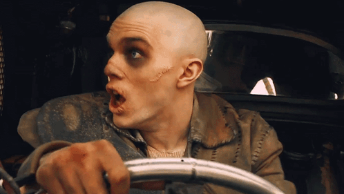 A Man With A Shaved Head Is Holding A Steering Wheel With His Mouth Open GIF
