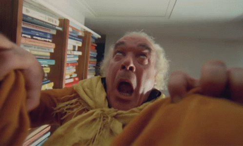 A Man With A Shocked Look On His Face Is Standing In Front Of A Bookshelf Full Of Books GIF